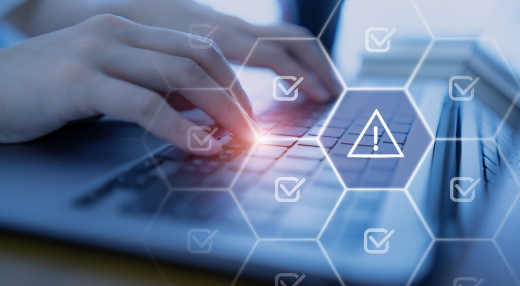 Hands typing on a laptop keyboard with a warning alert icon, representing system risks that contribute to the cost of IT downtime.